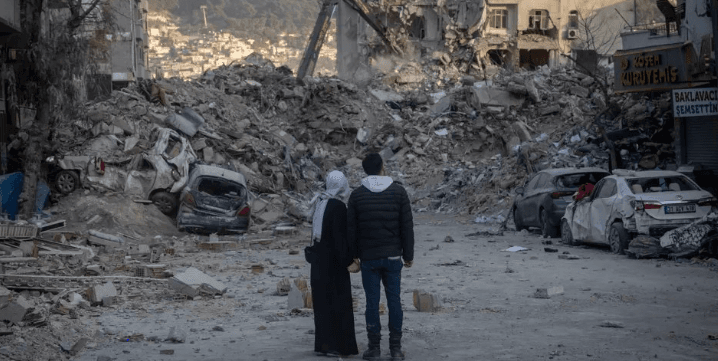 Deprem bölgesinde enkazın önünde duran iki kişi.