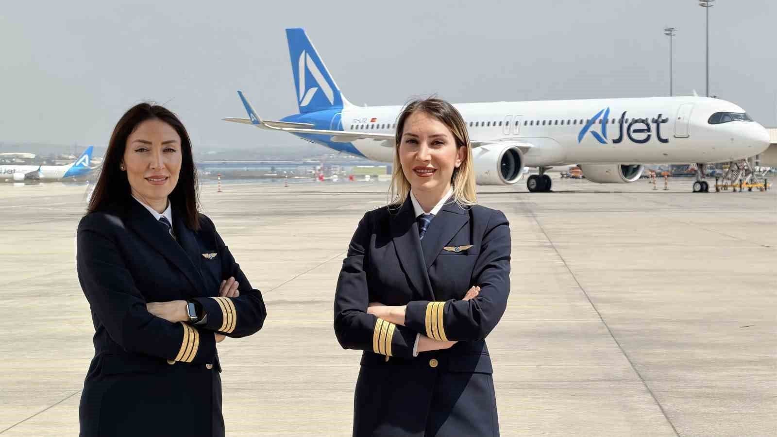Havalimanı pistinde bir AJet uçağının önünde duran iki kadın pilot.