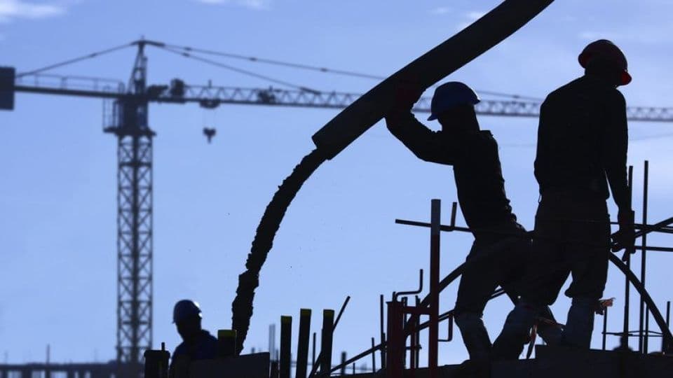 Bir inşaat sahasında beton döken işçilerin silüeti ve arka planda görünen vinç.