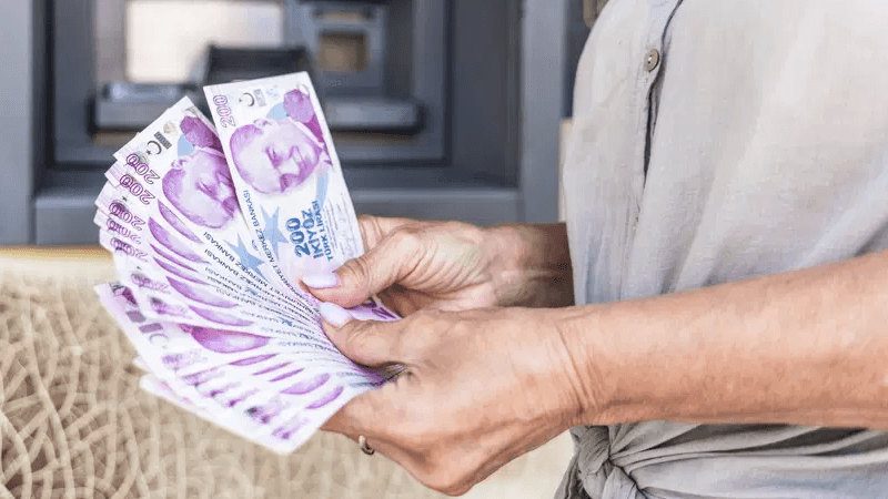 Bir kişinin elinde Türk Lirası banknotları, arka planda ATM. Emekli promosyonları.