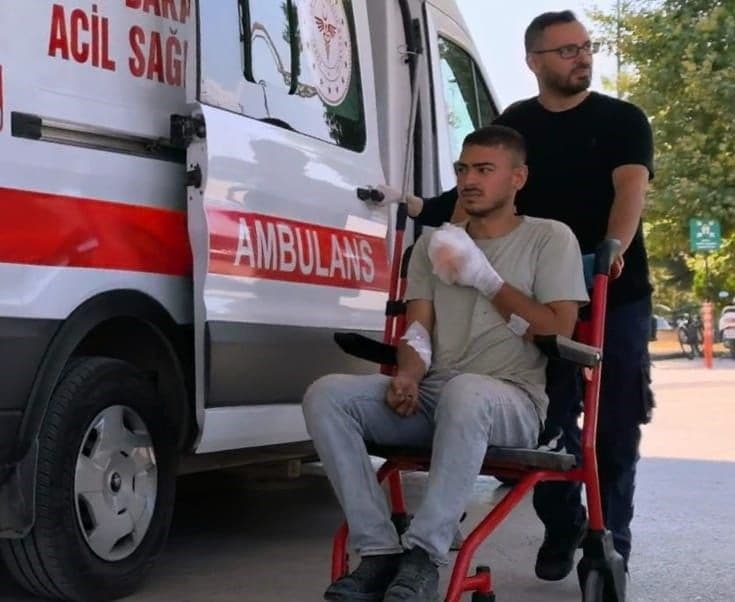 Domaniç'te iş kazası geçiren ve parmakları sargılı olan genç, tekerlekli sandalyede ambulansın yanında görülüyor.