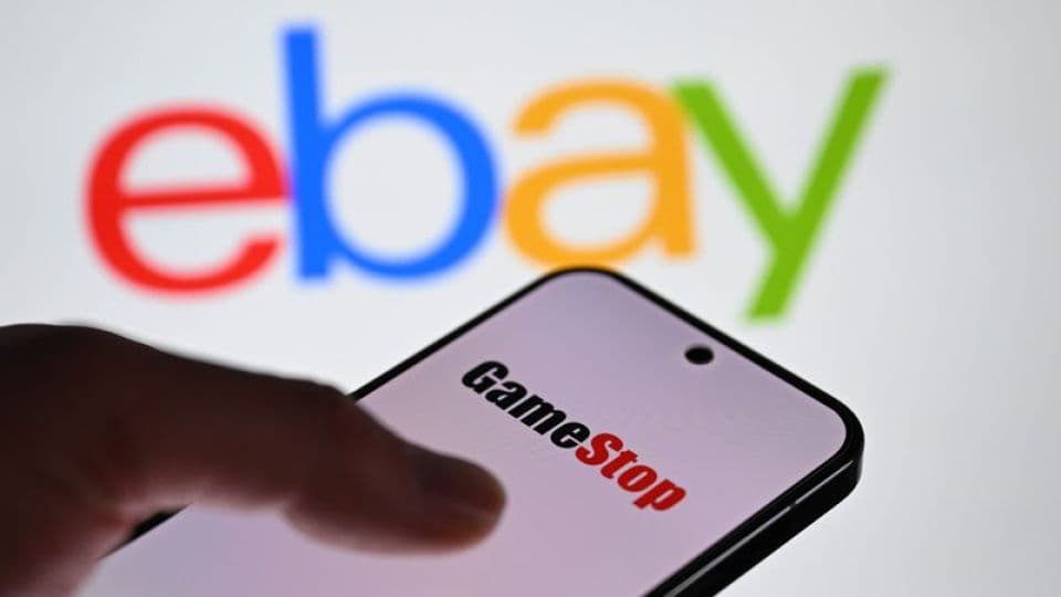 Akıllı telefonda GameStop logosu ve arka planda bulanık eBay logosu.