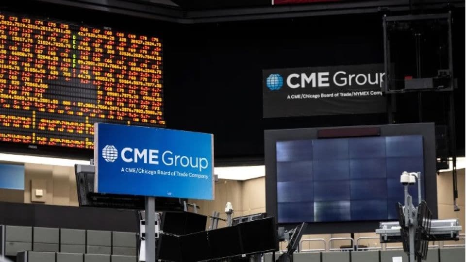 CME Group borsa işlem katından bir görünüm, ekranlarda finansal veriler ve şirketin logosu yer alıyor.