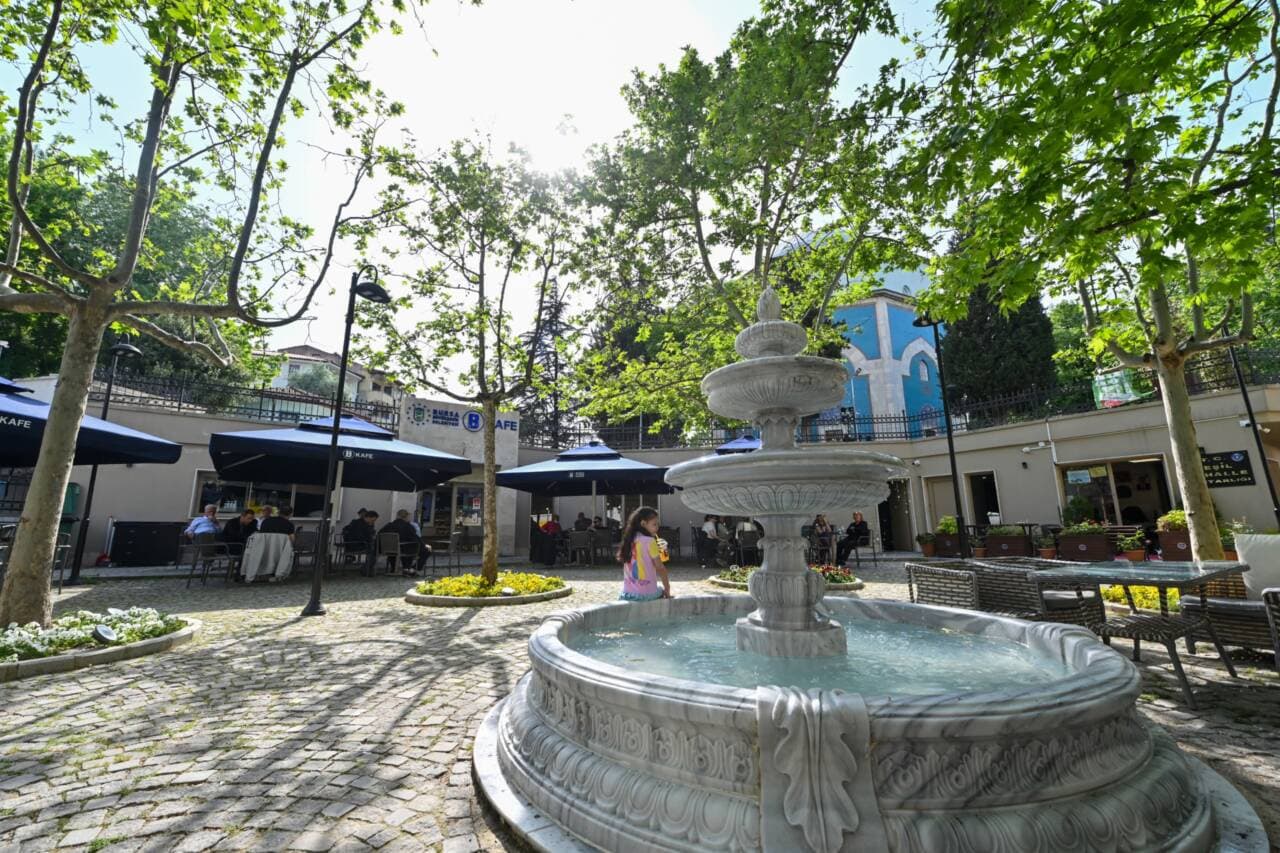 Bursa'da bir BURFAŞ B Kafe'nin fıskiyeli ve ağaçlıklı avlusunda oturan insanlar.
