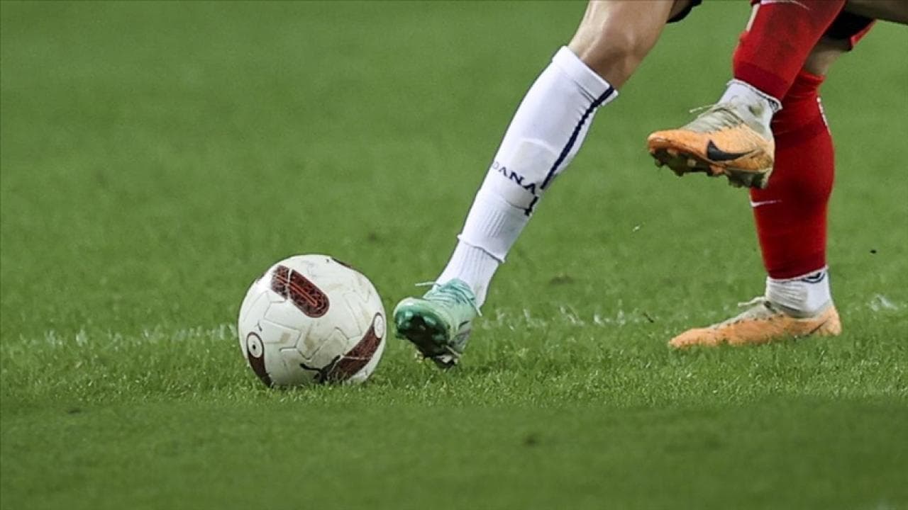 Futbol sahasında topa müdahale eden iki futbolcunun bacakları ve futbol topu.