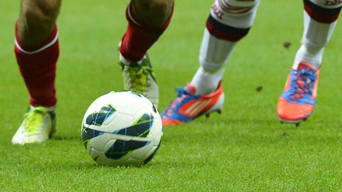 Yeşil çim sahada futbol topu ve futbolcuların bacakları.