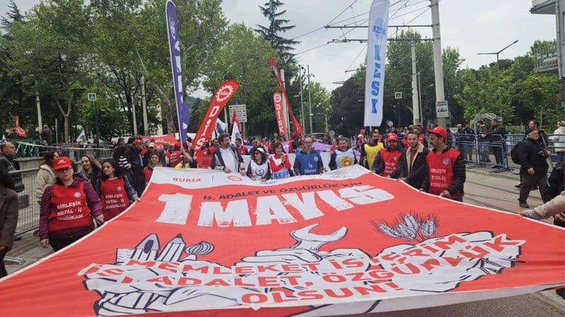 Bursa'da 1 Mayıs Emek ve Dayanışma Günü kutlamalarından bir görüntü, sendika bayrakları taşıyan işçiler yürüyor.