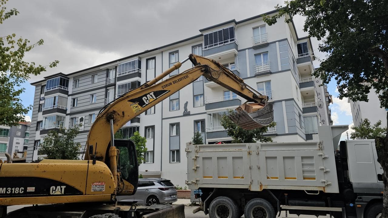Çorum Belediyesi ekipleri, bir apartmanın önünde iş makinesiyle çöp evden atıkları kamyona yüklüyor.