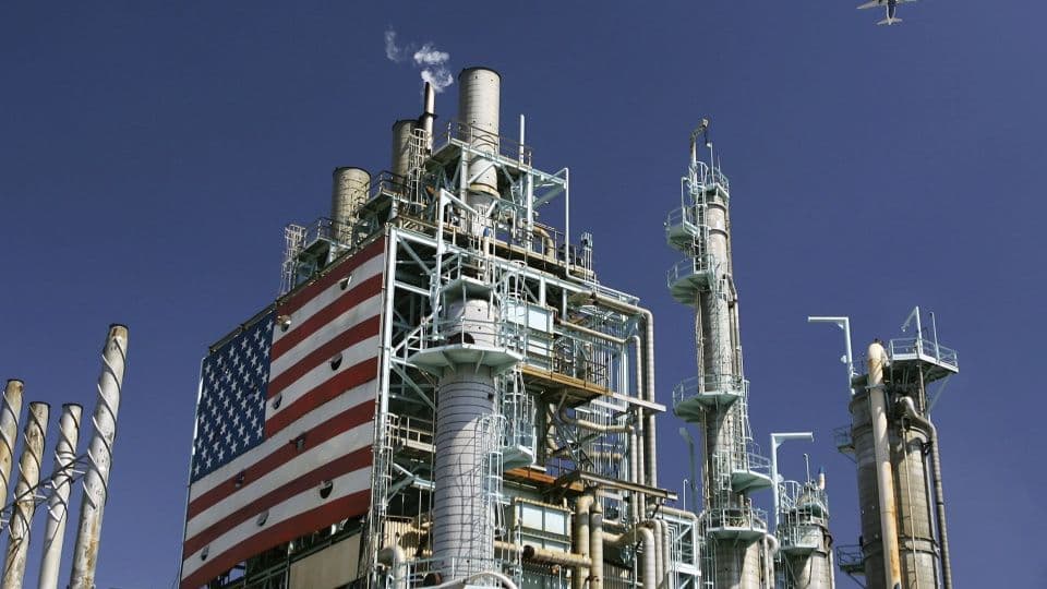 Üzerinde büyük bir Amerikan bayrağı bulunan bir petrol rafinerisinin endüstriyel yapısı ve bacaları.