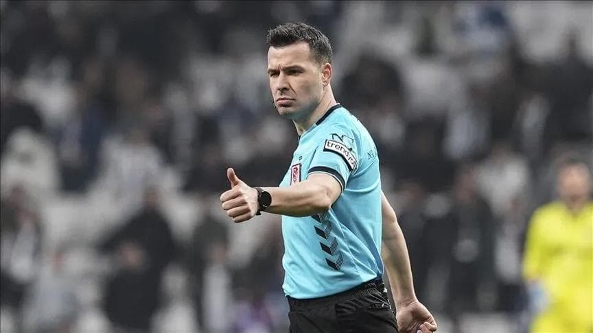 FIFA kokartlı hakem Cihan Aydın, futbol sahasında başparmağı yukarıda poz veriyor.