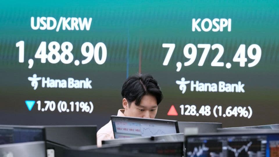 Güney Kore borsası KOSPI endeksini gösteren bir ekran ve önünde bilgisayarına bakan bir borsa çalışanı.
