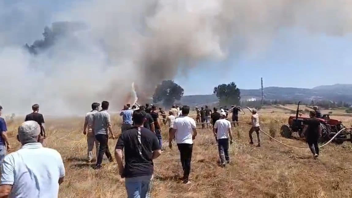 Bursa Orhaneli'de çıkan tarla yangınına müdahale eden mahalle sakinleri ve yükselen dumanlar.