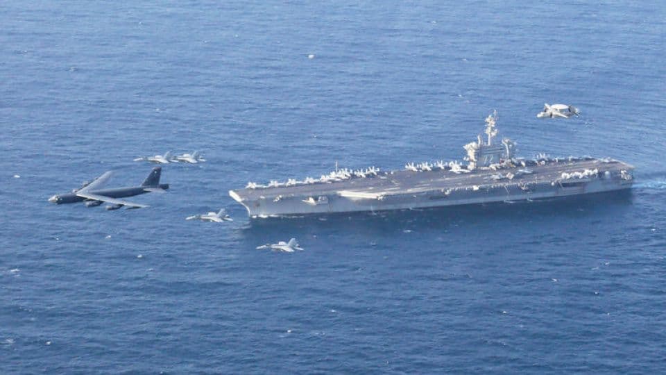 Okyanusta seyreden uçak gemisi, bombardıman uçağı ve savaş jetleri, ABD-İsrail-İran gerilimi.