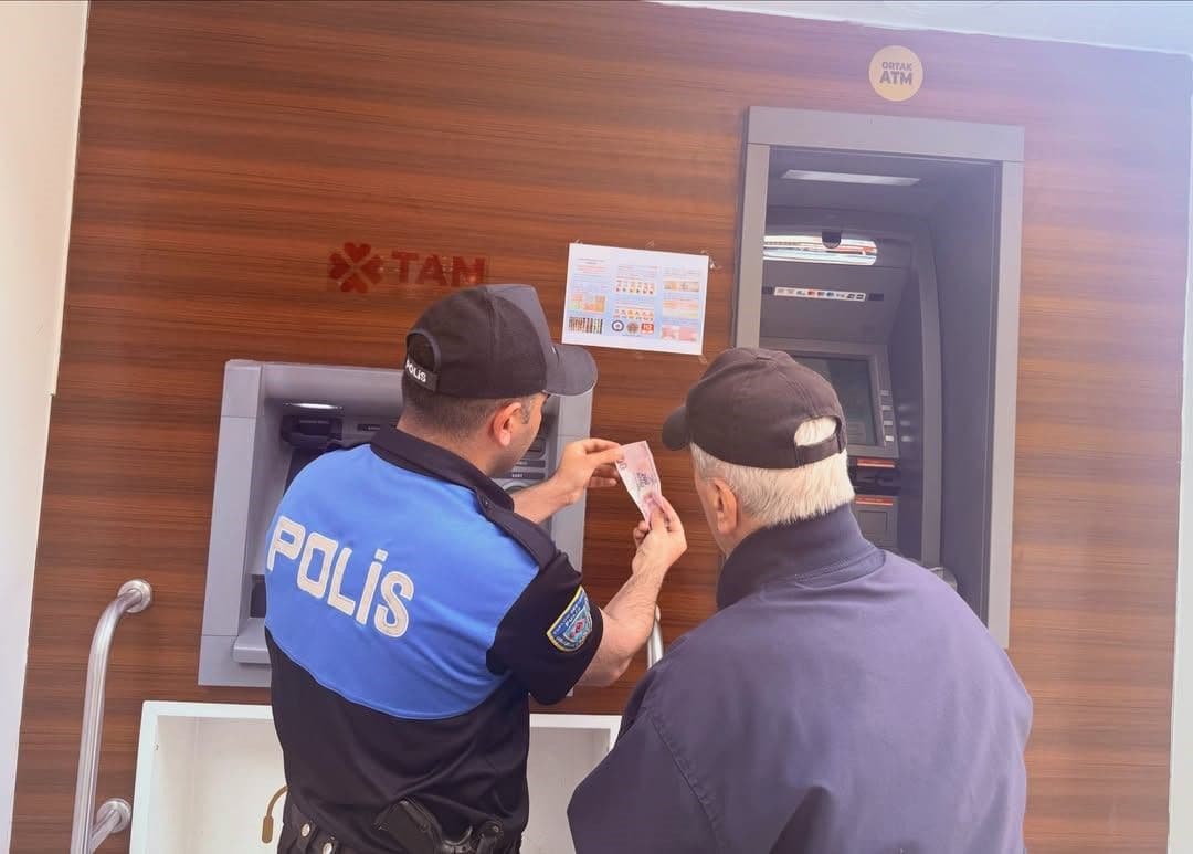 Bilecik'te bir polis memuru, ATM önünde bir vatandaşa sahte para konusunda bilgi veriyor.