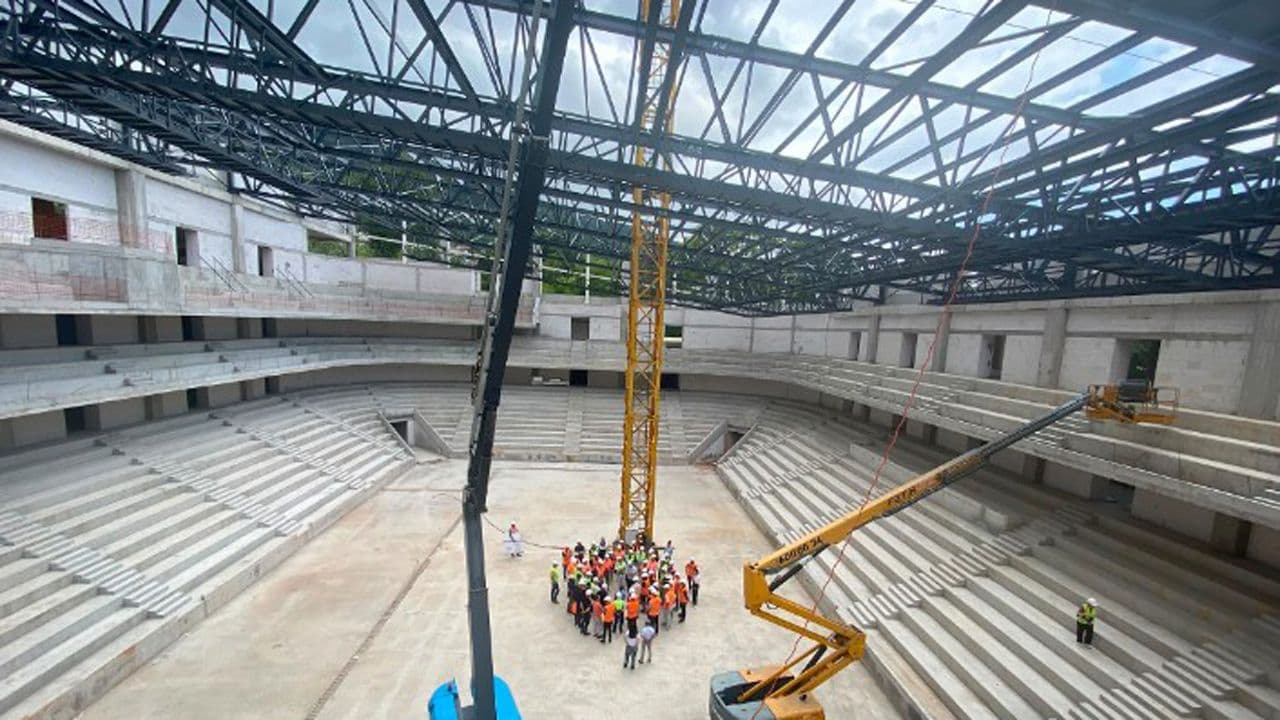 Bursa Atatürk Spor Salonu inşaatının iç görünümü, tribünler, çelik çatı yapısı ve şantiyede toplanmış bir grup insan.