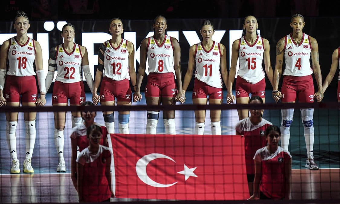 A Milli Kadın Voleybol Takımı oyuncuları, sahada Türk bayrağı önünde el ele duruyor.