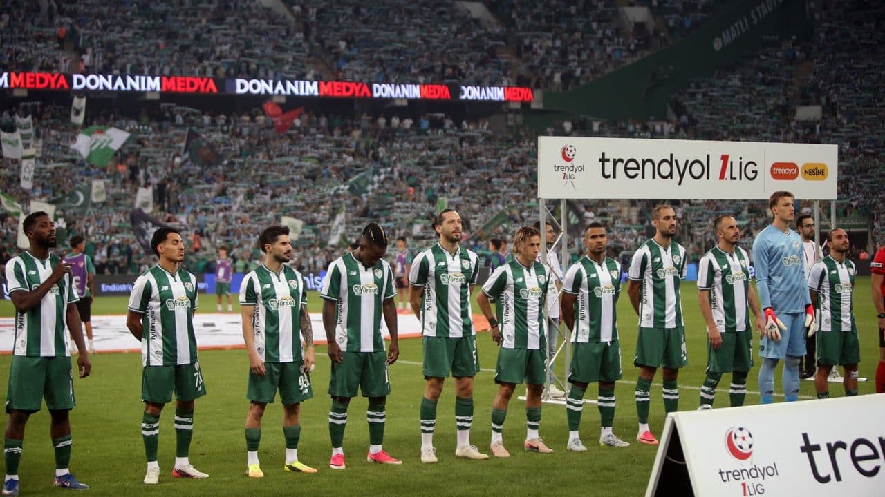 Bursasporlu futbolcular sahada, tribünlerde coşkulu taraftarlar.