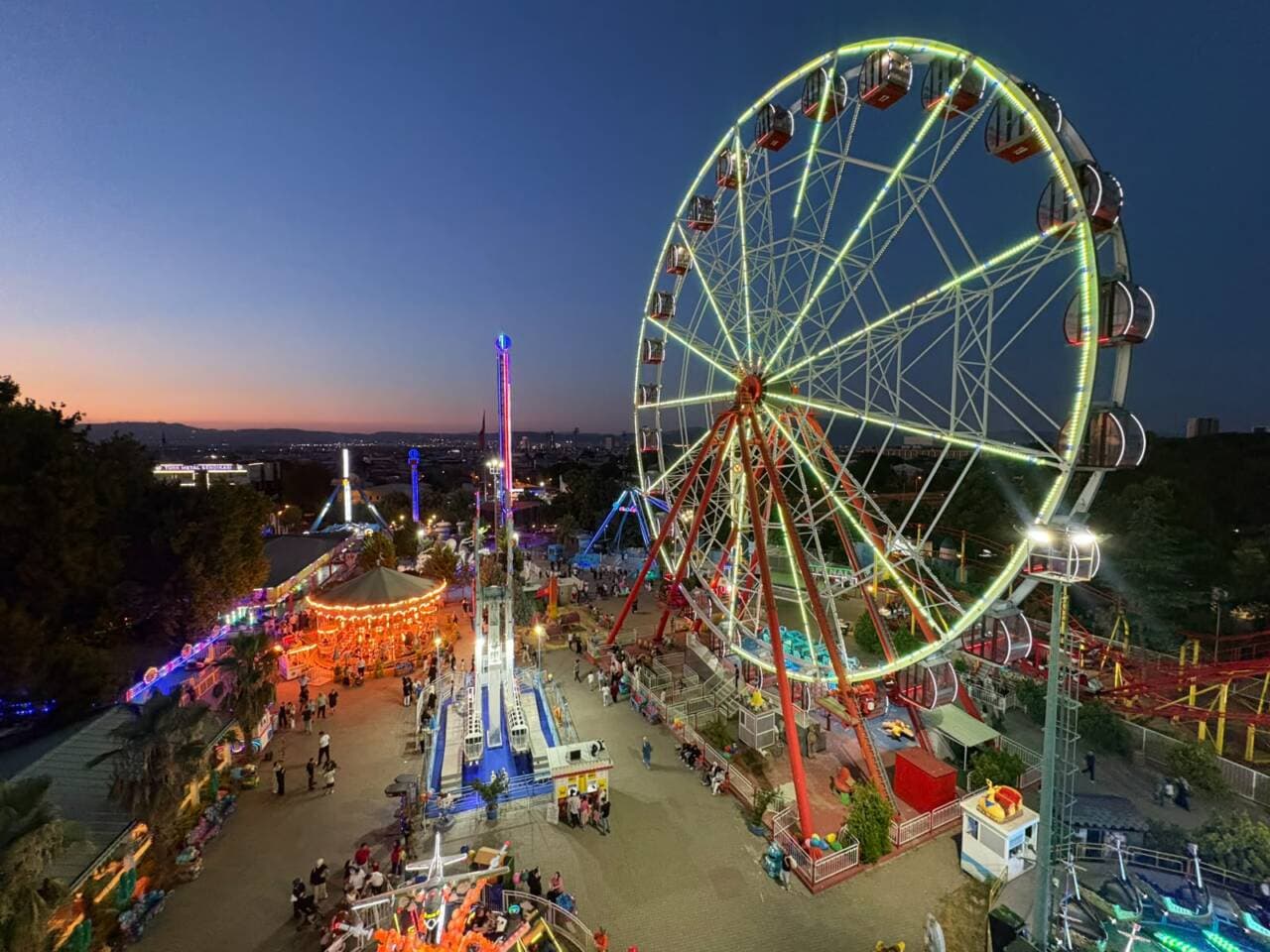 Bursa Kültürpark Lunaparkı'nın akşam görünümü, ışıklandırılmış dönme dolap ve diğer eğlence üniteleri.