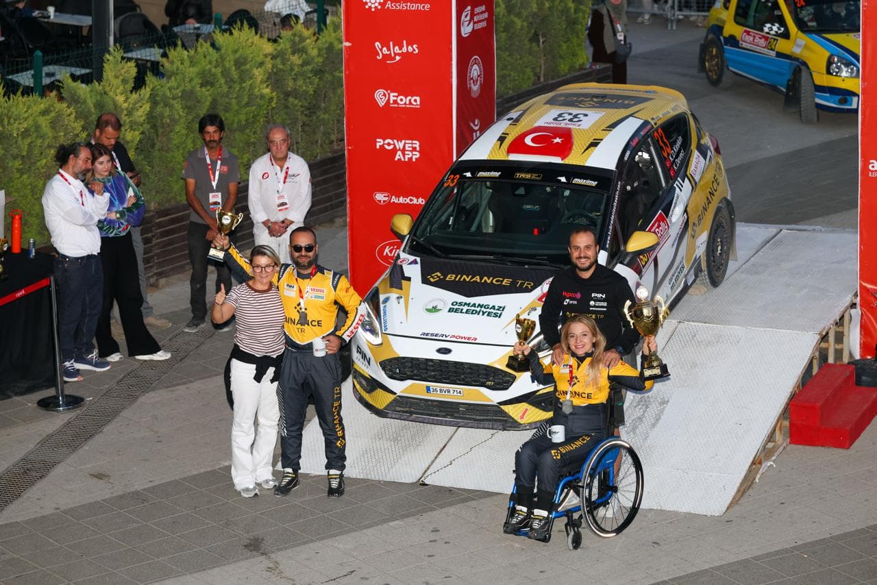 Kübra Denizci Keskin ve co-pilotu Kerem Deveci, ralli aracının önünde kupalarıyla poz veriyor.