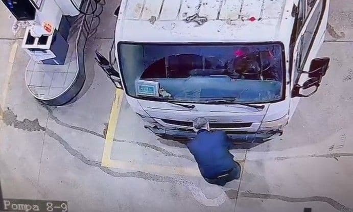 Güvenlik kamerası görüntüsünde bir kişi kamyonun ön tamponuna eğilmiş bir şeyler yapıyor.