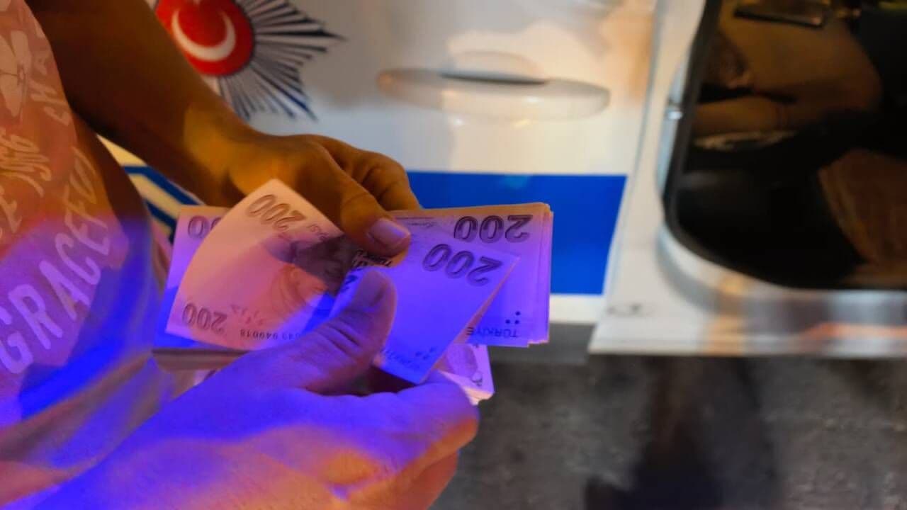Polis aracının önünde elinde Türk lirası banknotları tutan bir kişi.