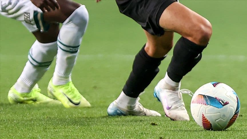 Futbol sahasında iki futbolcunun ayakları ve top.