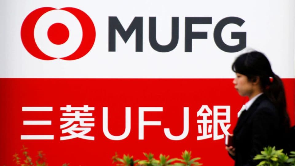 Mitsubishi UFJ Financial Group (MUFG) bankasının logosu ve önünden geçen bir kişi.