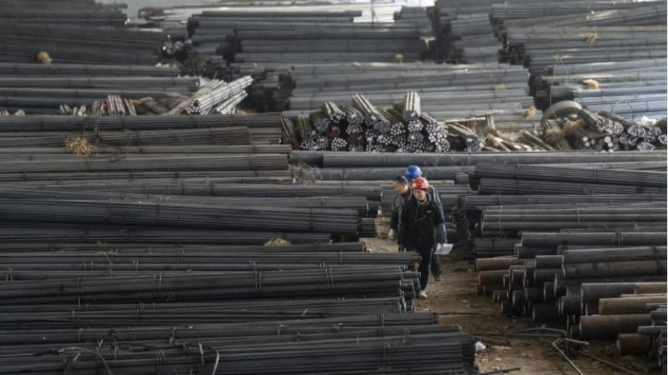 Çin'de bir çelik fabrikasının deposunda yığılmış çelik çubuklar ve baretli işçiler.
