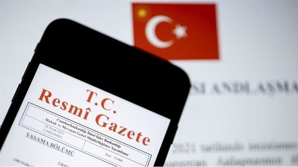 Resmi Gazete'nin bir akıllı telefon ekranında görüntüsü ve arka planda Türk bayrağı.
