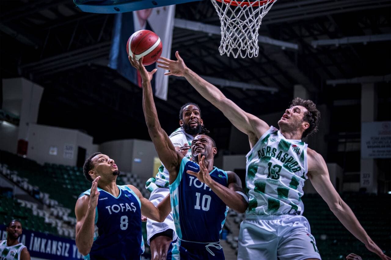 Bursaspor ve TOFAŞ arasında oynanan bir basketbol maçından enstantane, oyuncular pota altında mücadele ediyor.