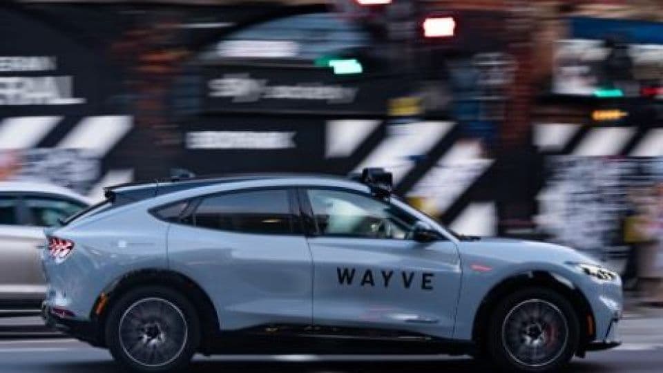 Şehirde hareket halinde olan Wayve logolu otonom sürüş aracı.
