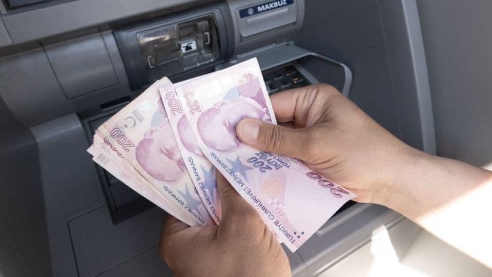 ATM önünde bir elin tuttuğu 200'lük Türk Lirası banknotları.