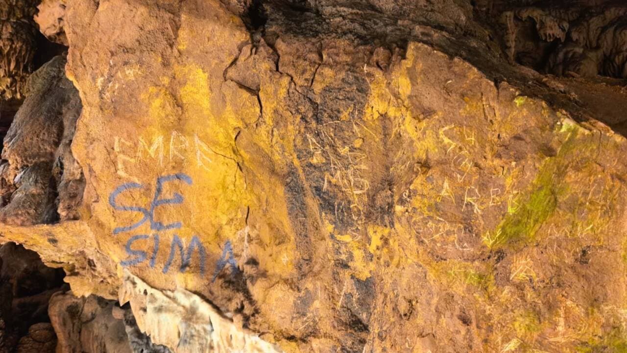 Oylat Mağarası duvarında sprey boya ve kazınmış yazılar, vandalizm izleri.
