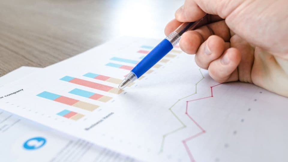 Bir elin kalemle finansal grafikler ve veriler içeren bir belgeyi incelemesi.