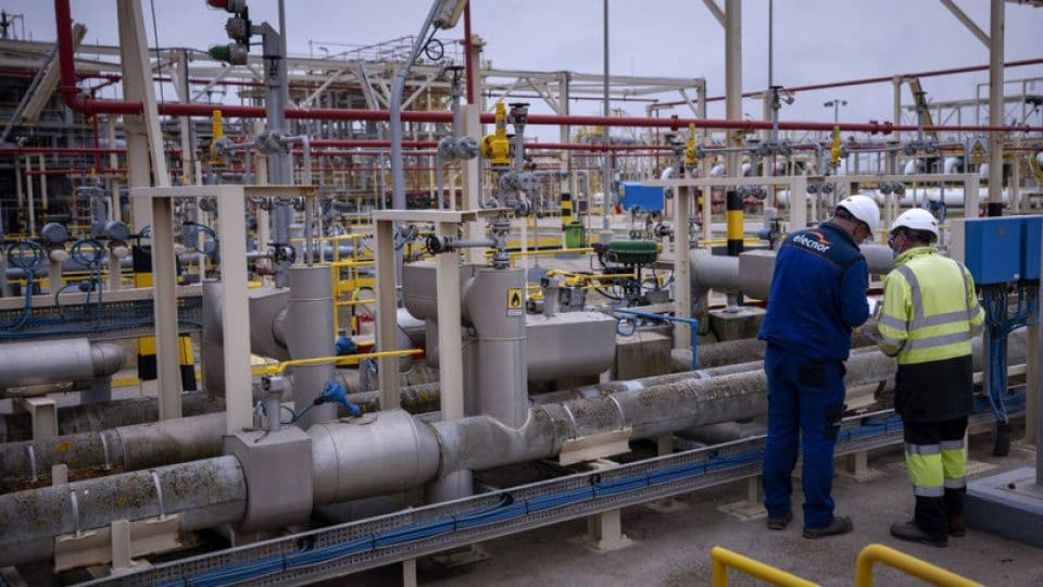Doğalgaz tesisinde boru hatları ve vanalar arasında çalışan iki işçi.