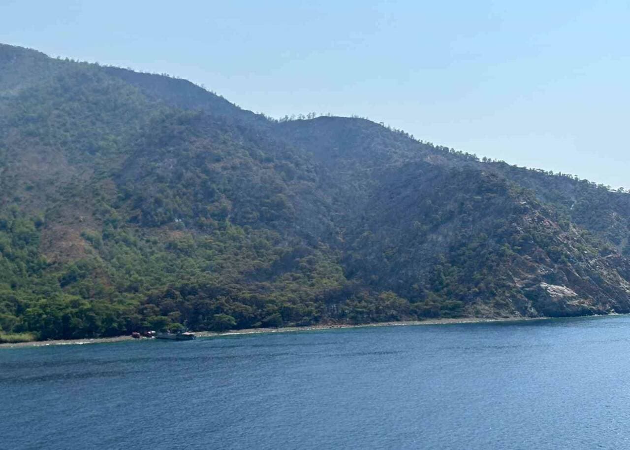 Marmaris'teki orman yangını sonrası denizden görünüm, yanan ormanlık alanlar ve müdahale gemileri.