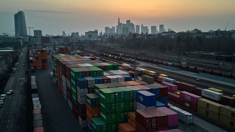 Uluslararası ticaretin sembolü olan nakliye konteynerleri ve bir şehir silüeti.