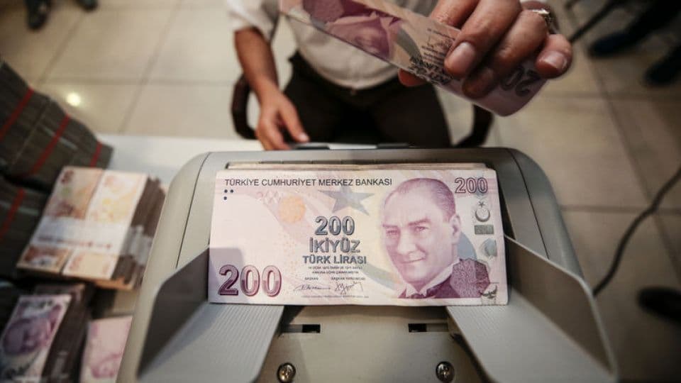 Para sayma makinesinde duran 200 Türk Lirası banknotu ve arka planda para desteleri.