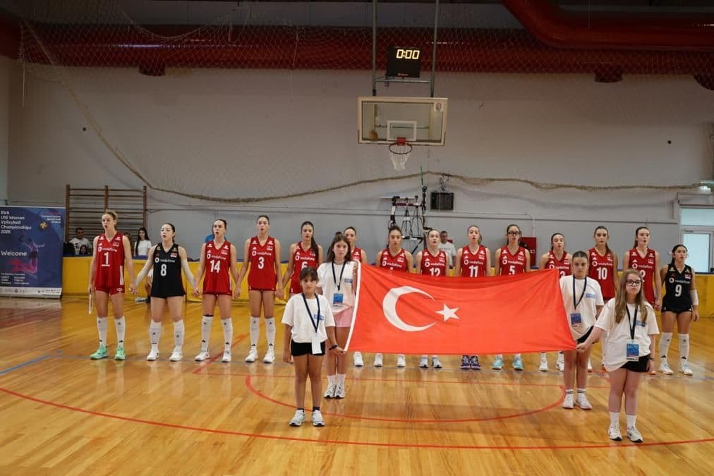 Türkiye U16 Milli Voleybol Takımı oyuncuları, Türk bayrağı ile sahada dizilmiş duruyor.