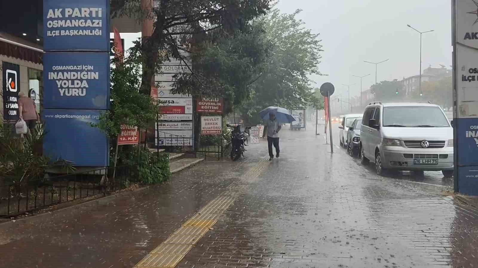 Bursa'da sağanak yağış sonrası su basan cadde, şemsiyeli bir kişi ve trafikteki araçlar.