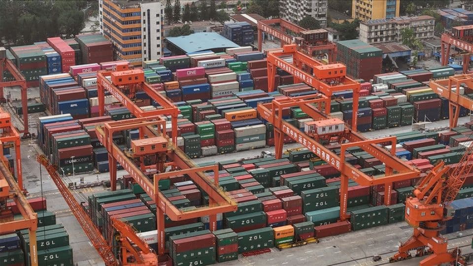 Bir limanda üst üste dizilmiş konteynerler ve vinçler, küresel ticareti simgeliyor.