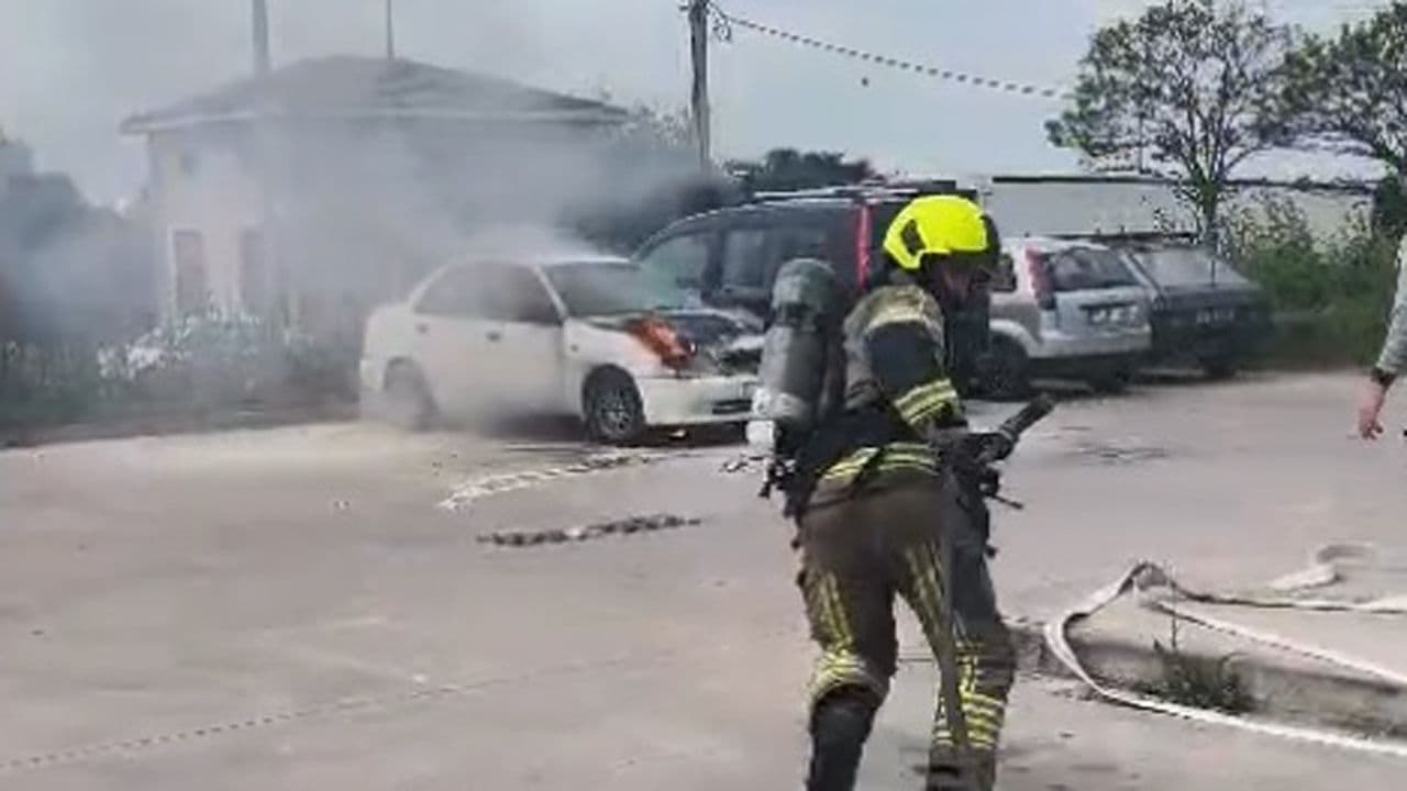 Karacabey Devlet Hastanesi otoparkında yanan otomobil ve müdahale eden itfaiye ekibi.