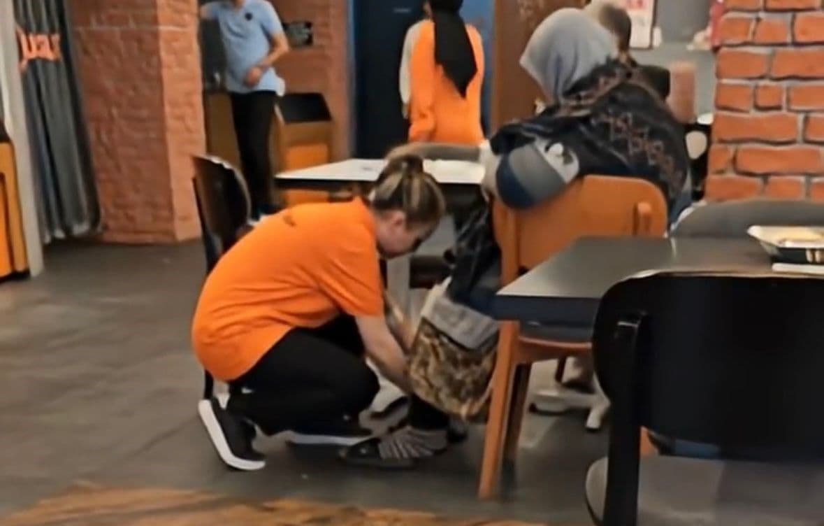 Köfteci Yusuf çalışanı, restoranda yaşlı bir kadına çoraplarını giymesinde yardımcı oluyor.