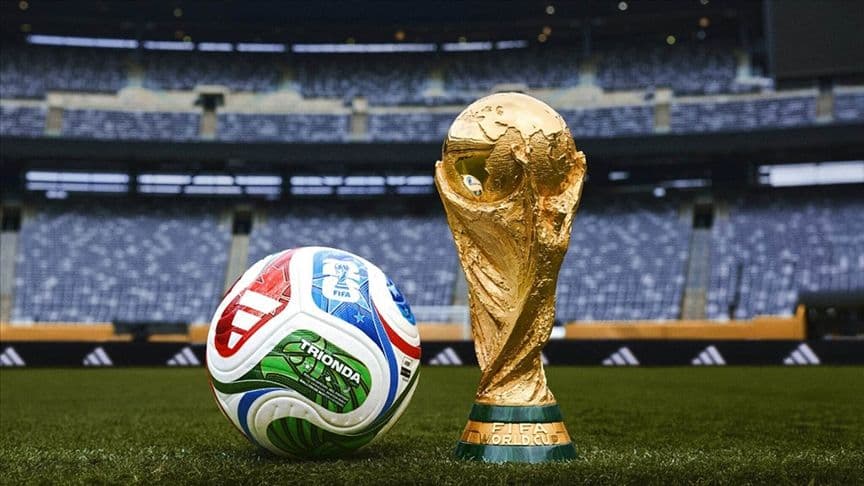 FIFA Dünya Kupası trofesi ve bir futbol topu, stadyumdaki çimlerin üzerinde duruyor.