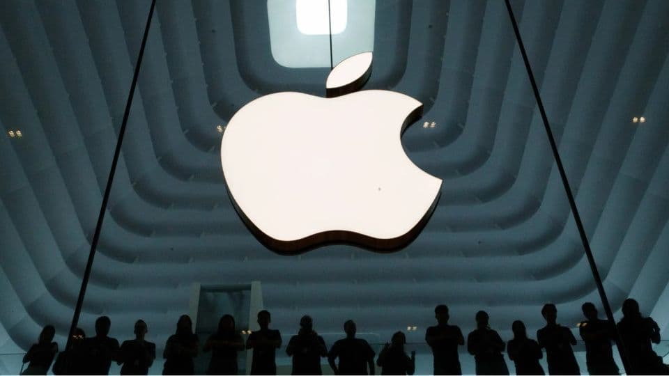 Bir Apple mağazasında asılı duran parlak Apple logosu ve aşağıda duran insan silüetleri.