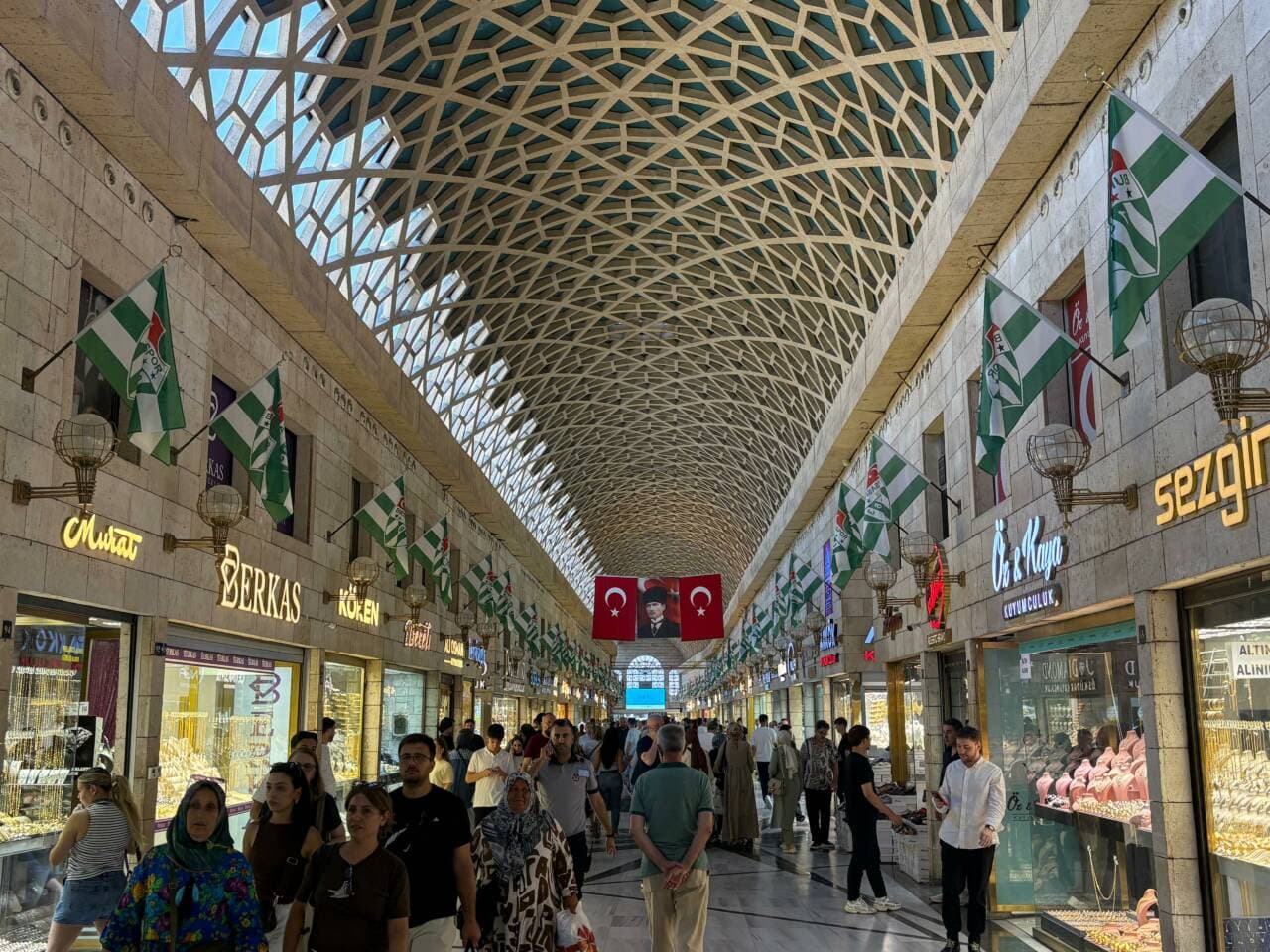 Bursa Kapalı Çarşı'da Bursaspor bayraklarıyla süslenmiş dükkanlar ve çarşıda yürüyen insanlar.