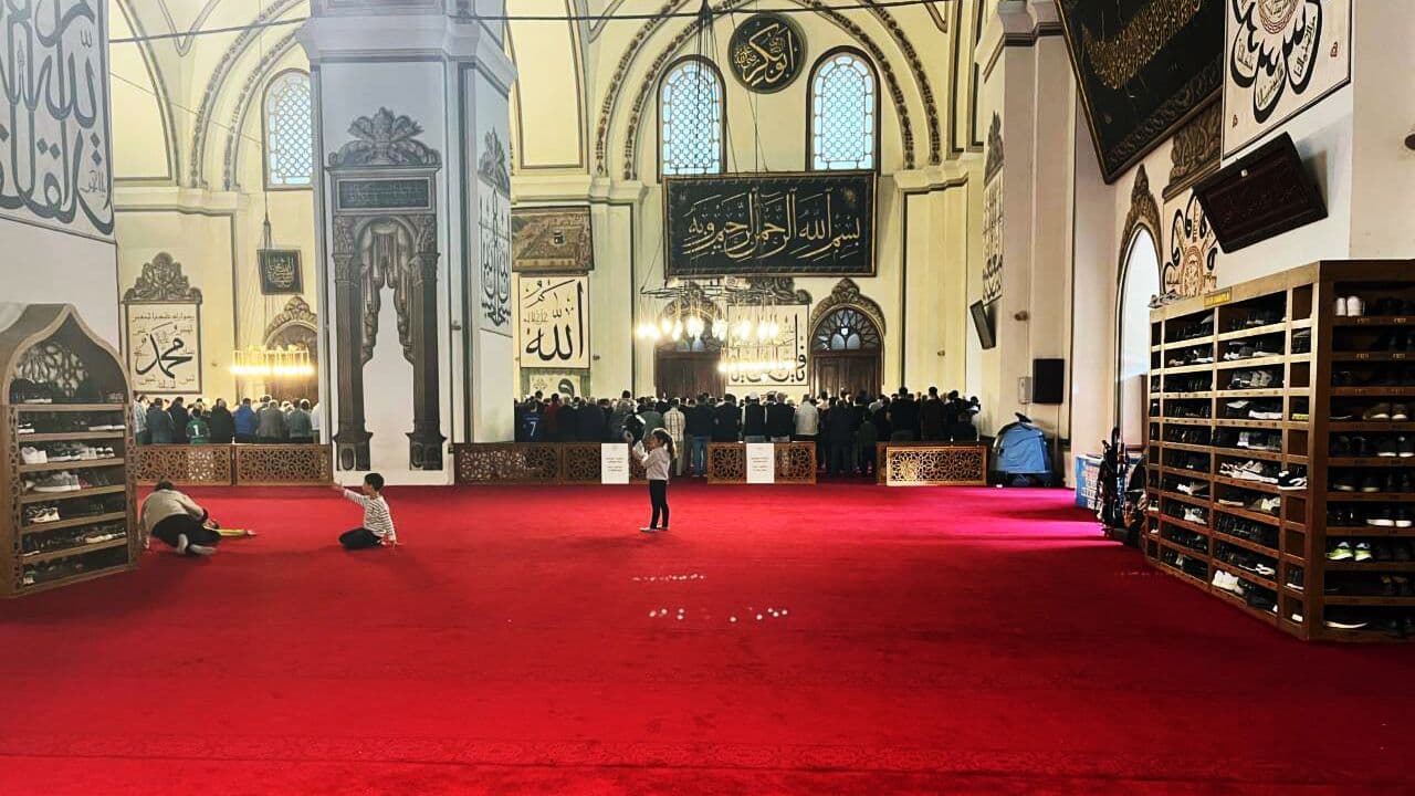 Bursa Ulucami'nin içinde, yeni serilmiş kırmızı halılar ve ibadet eden cemaat.