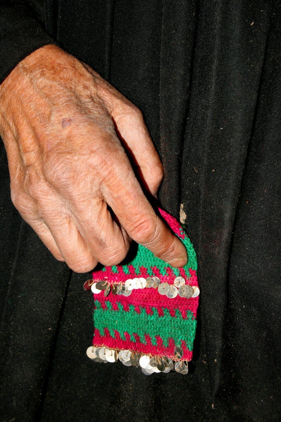 Yaşlı bir el, geleneksel el işi nakışlı ve pullu kumaşı tutuyor. El emeği göz nuru ürünlerin kültürel mirasını temsil ediyor.